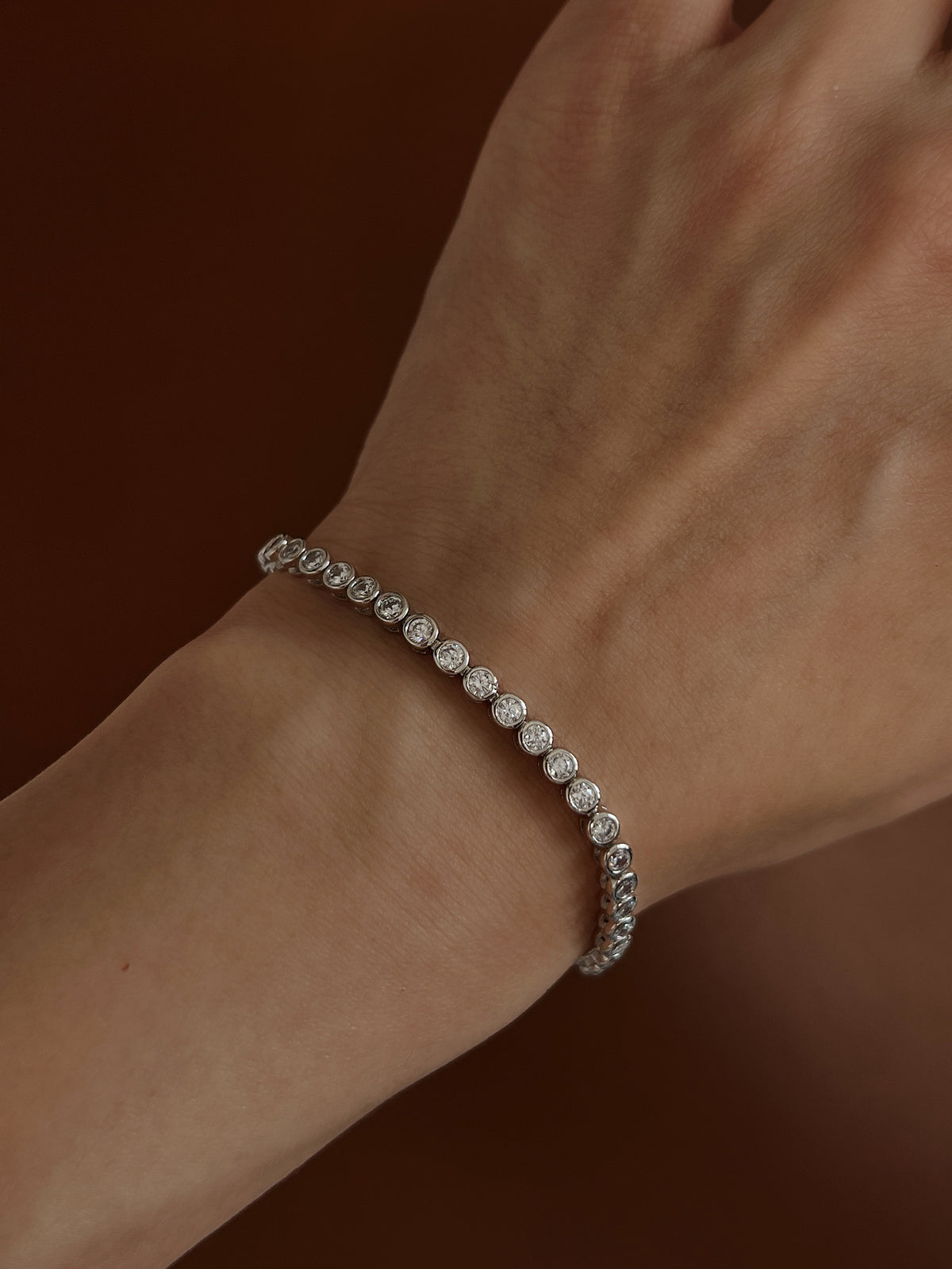 Cool sunlight highlighting the mirror-plated rhodium rims of a bezel tennis bracelet worn on a bare wrist.
