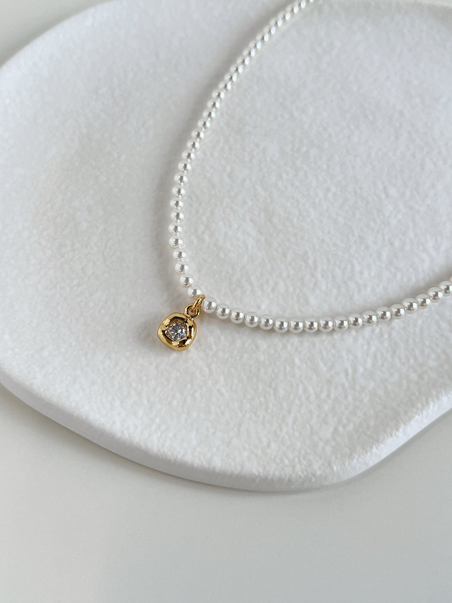 Still life jewelry composition emphasizing the contrast between reflective gold bezel metalwork and soft organic pearl surfaces