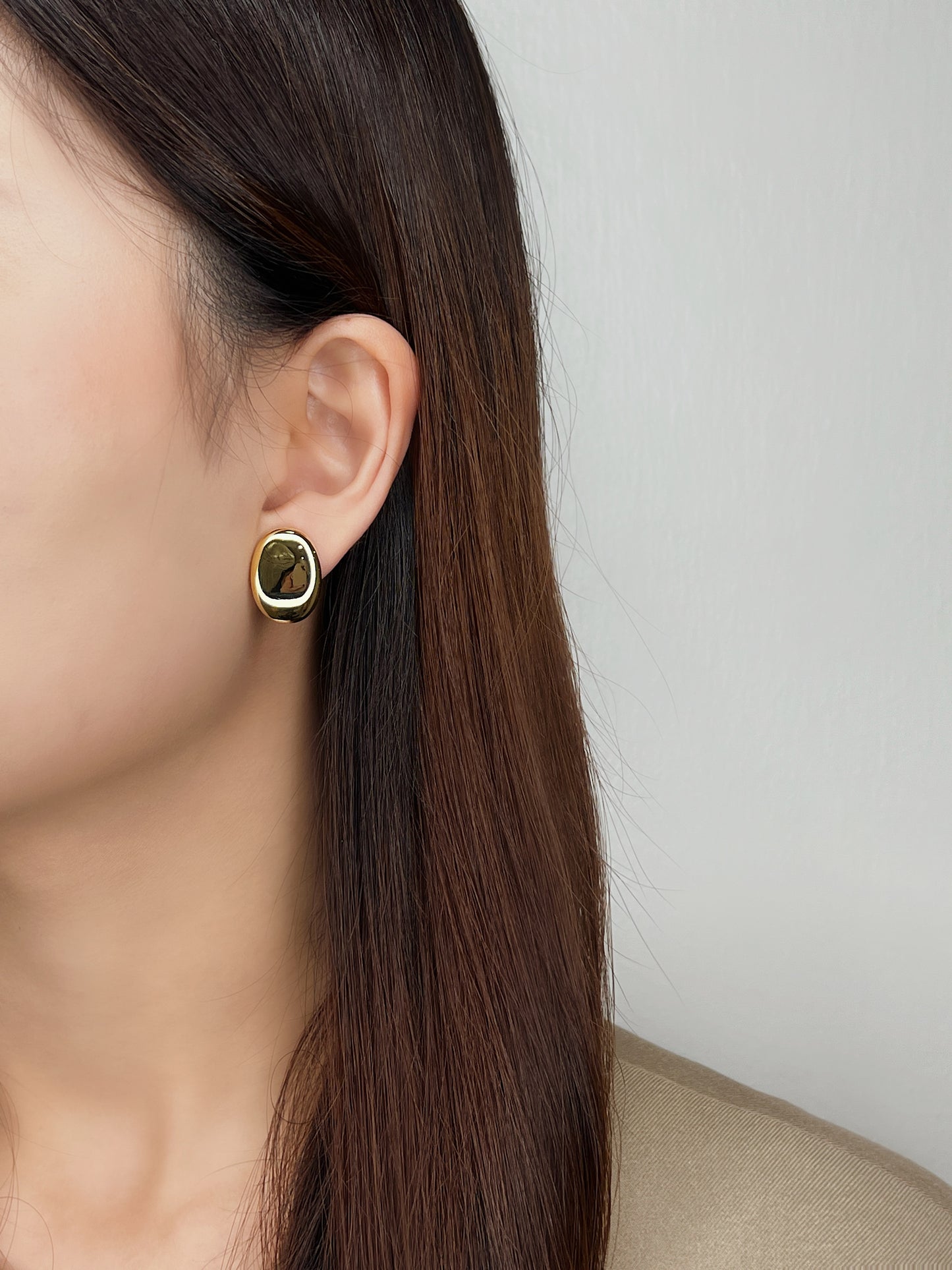 Studio shot of a model wearing chunky plain gold oval clip earrings with a contemporary beige blazer.