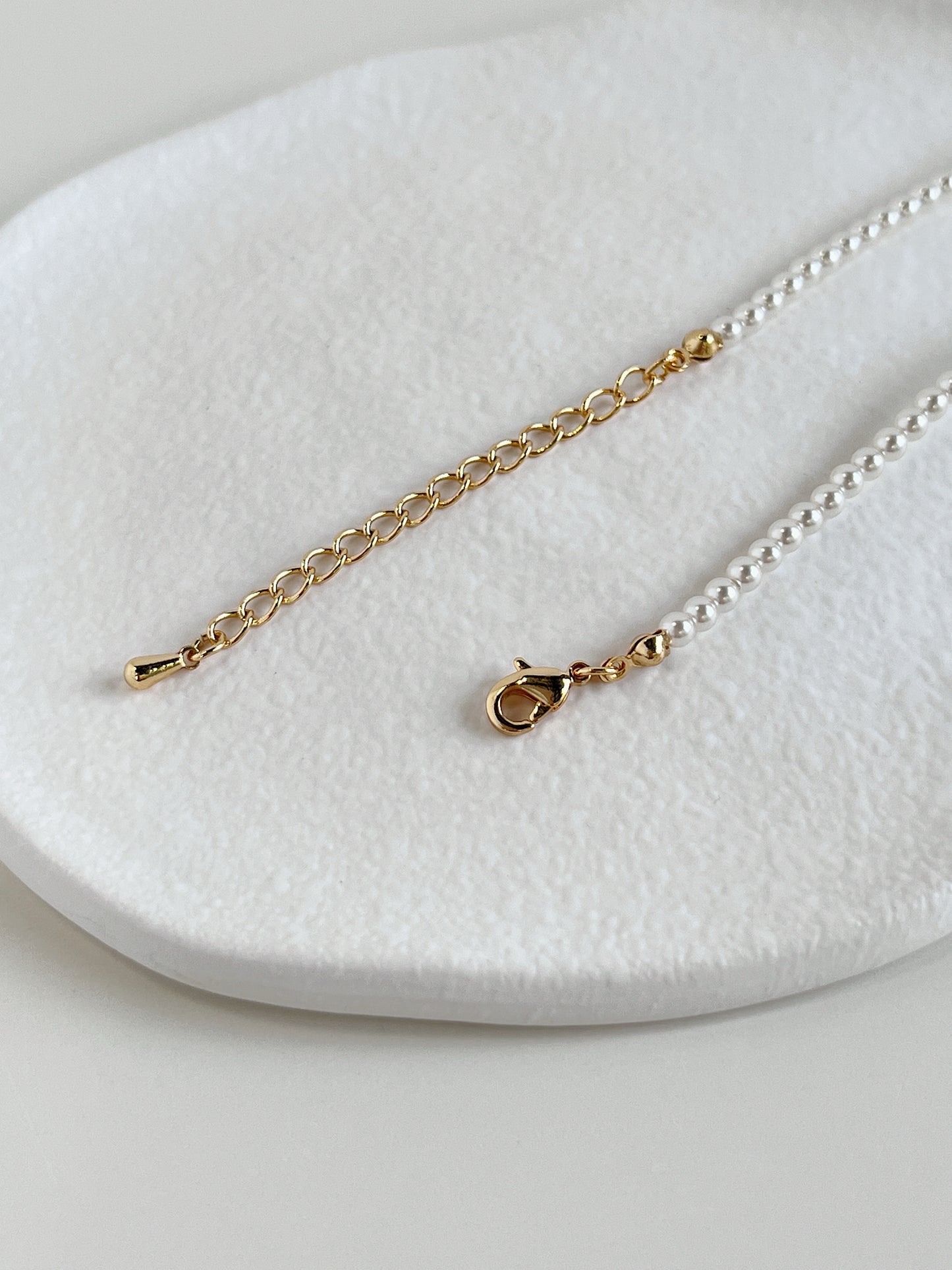 The 4mm micro pearl choker laid out in a crescent curve to display its supple fluid drape and gold lobster closure