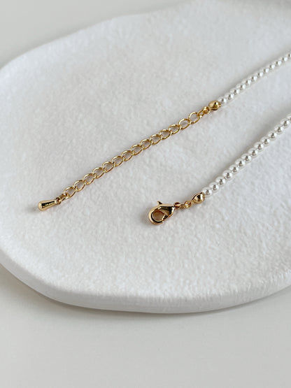 The 4mm micro pearl choker laid out in a crescent curve to display its supple fluid drape and gold lobster closure