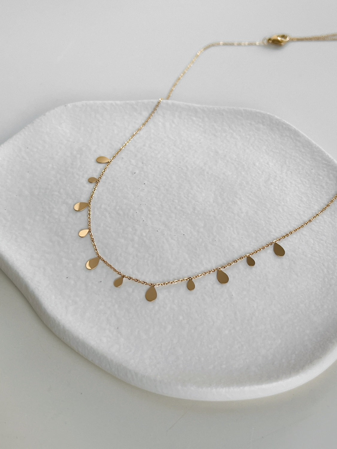 Close up view of high polish summer gold PVD organic pendant resting on fine steel link chain