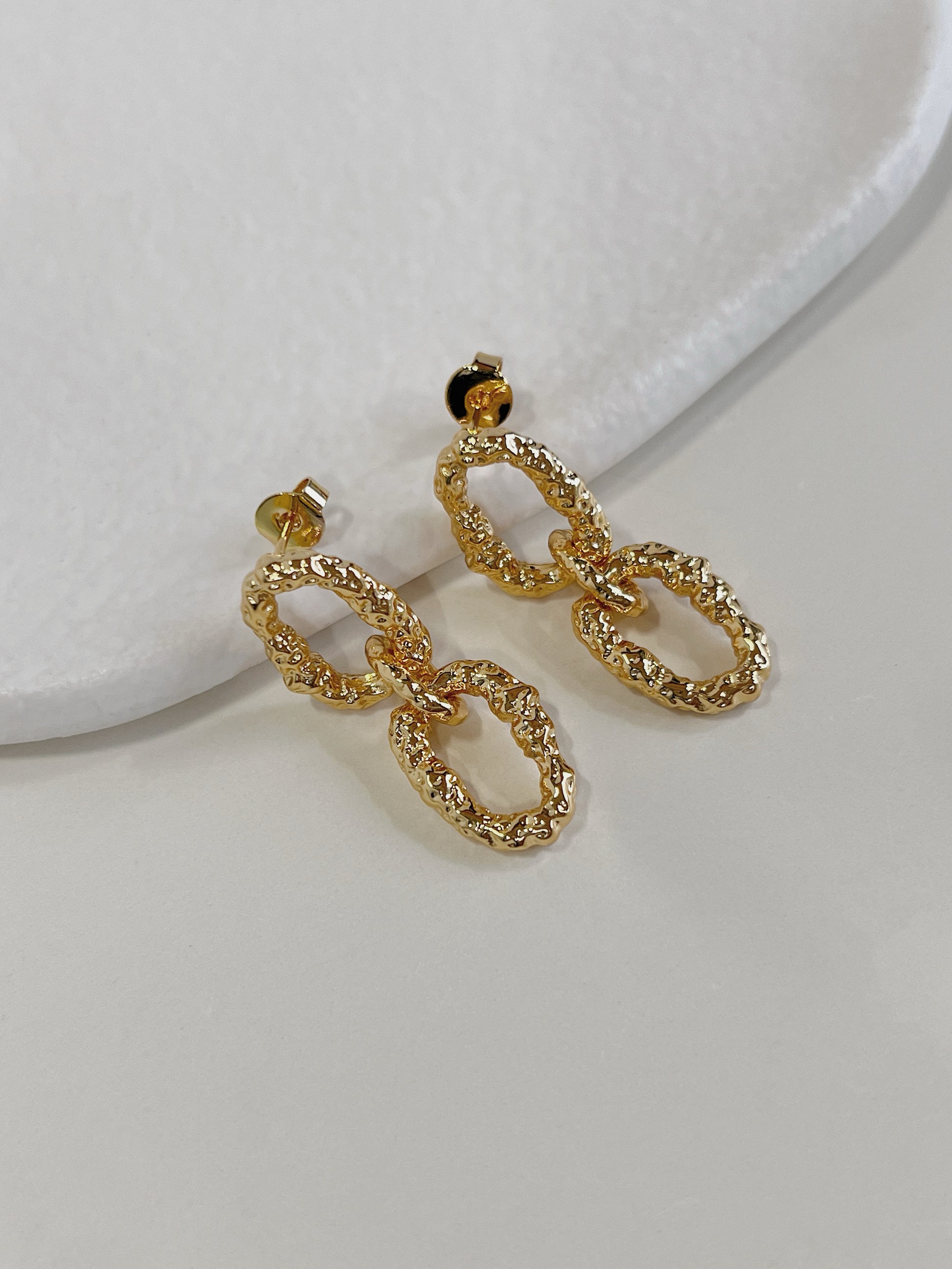 Close up perspective highlighting the crumpled textured hammered finish of 18k gold pvd drop earrings