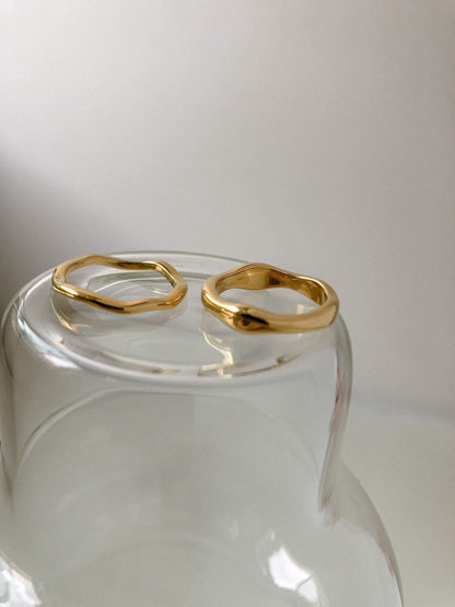 Side by side view of thick and slim wavy gold bands on glass surface.