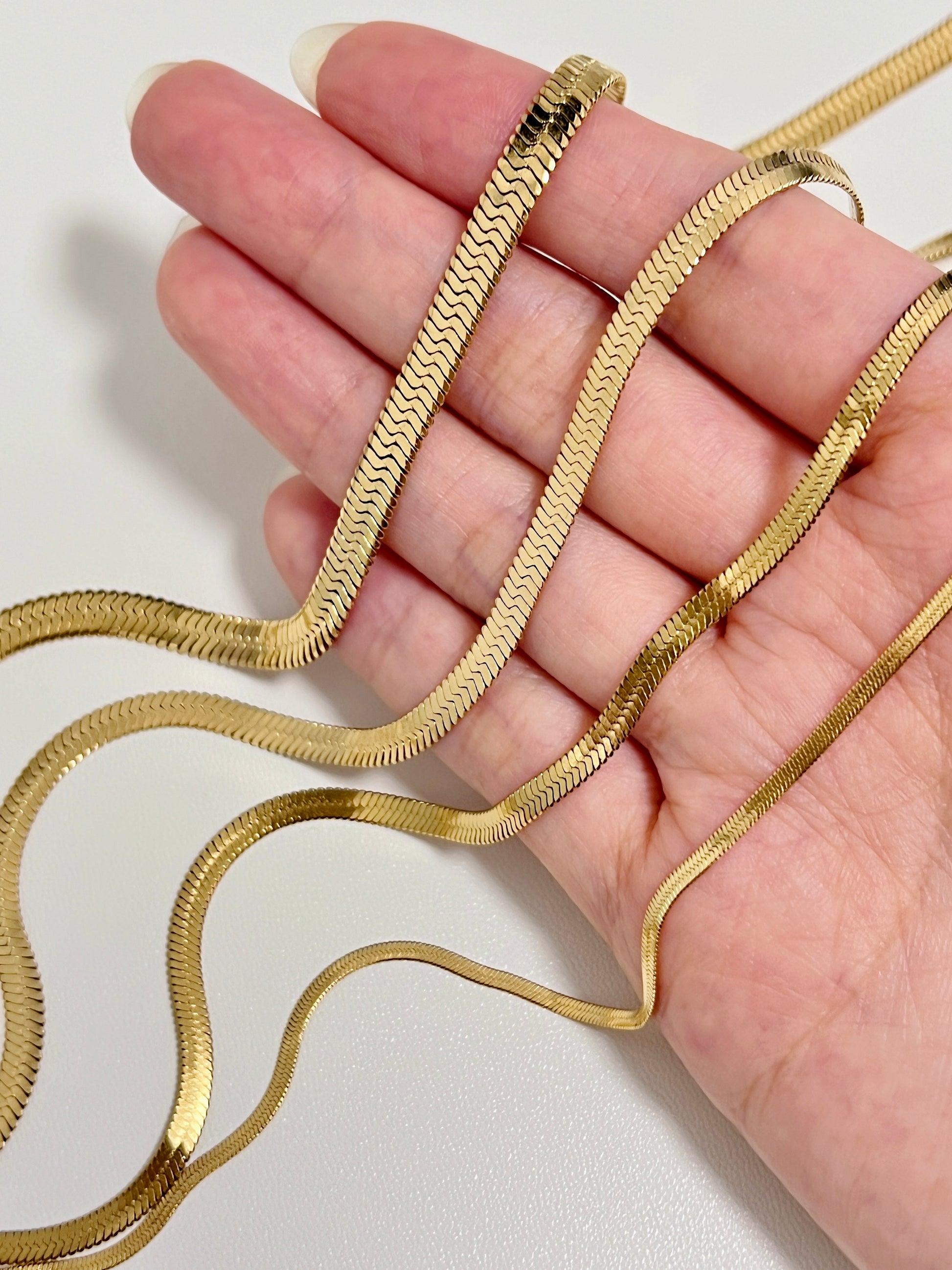 Studio product photo displaying a collection of gold tres snake chain necklaces in graduating widths across a hand