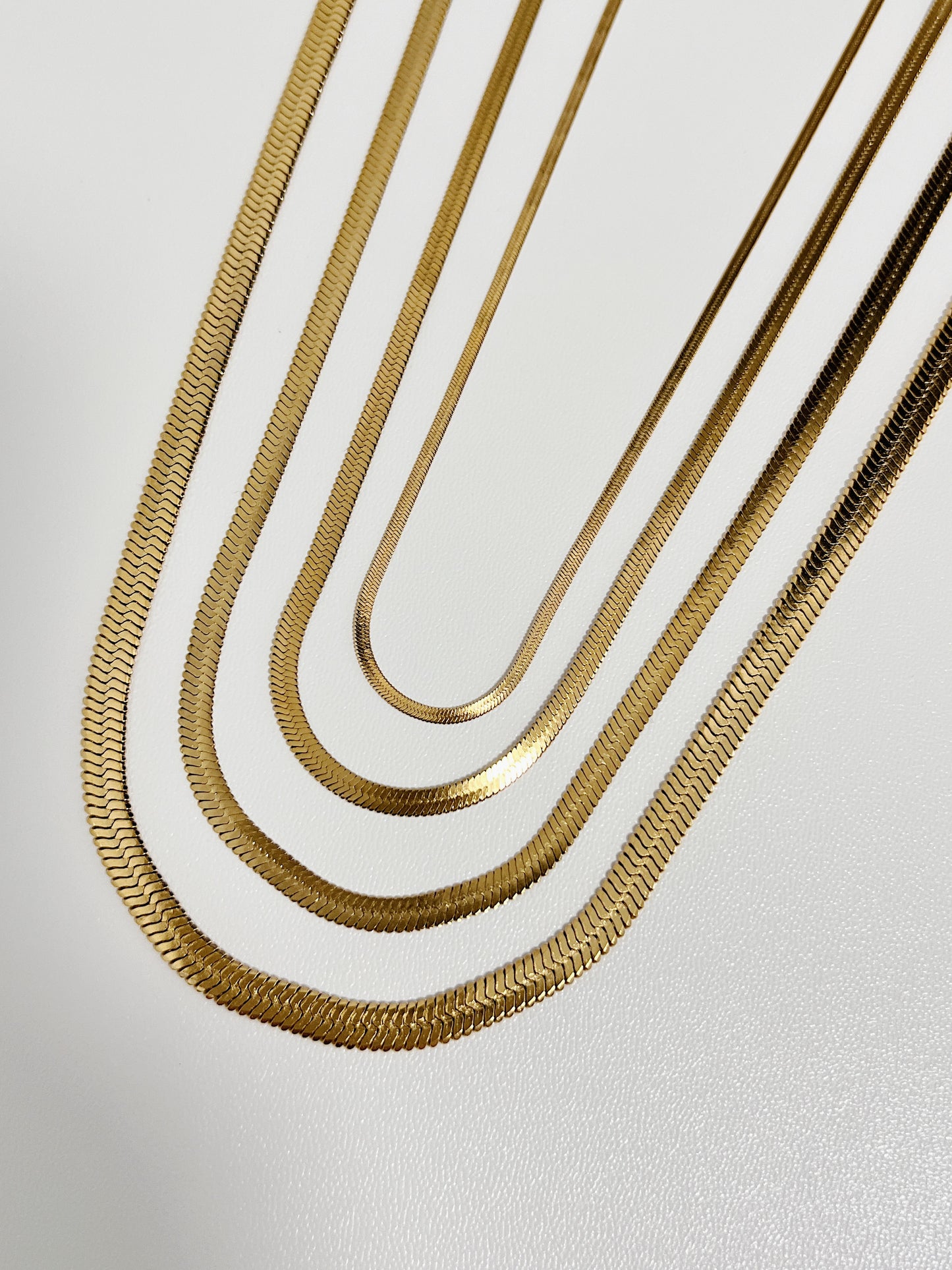 Parallel layout of flat herringbone chain necklaces highlighting the liquid mirror weave in different sizes