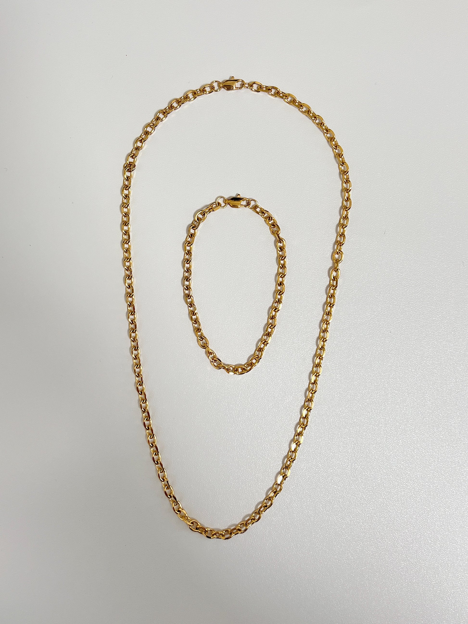 Studio layout displaying the Trixie cable chain bracelet nestled perfectly inside its matching luxury gold link necklace on a seamless white surface.