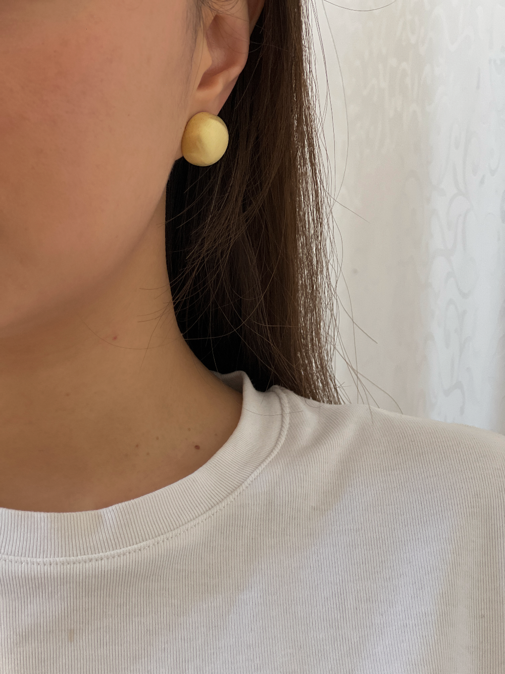 Close-up side profile of model wearing 16K gold plated Tyla brushed dome clip-on earring on unpierced ear