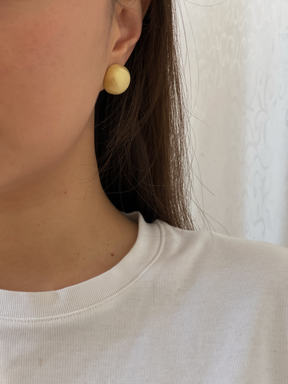 Close-up side profile of model wearing 16K gold plated Tyla brushed dome clip-on earring on unpierced ear