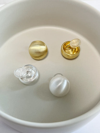 Flat lay inside a porcelain catchall displaying the hand-brushed satin surface and comfortable springless coil backs of both gold and silver dome clip-ons.