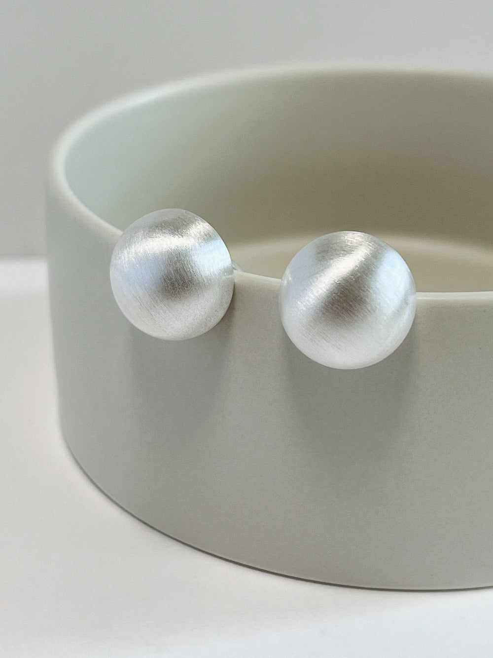 Pair of rhodium plated silver Tyla brushed dome clip-on earrings showing satin texture