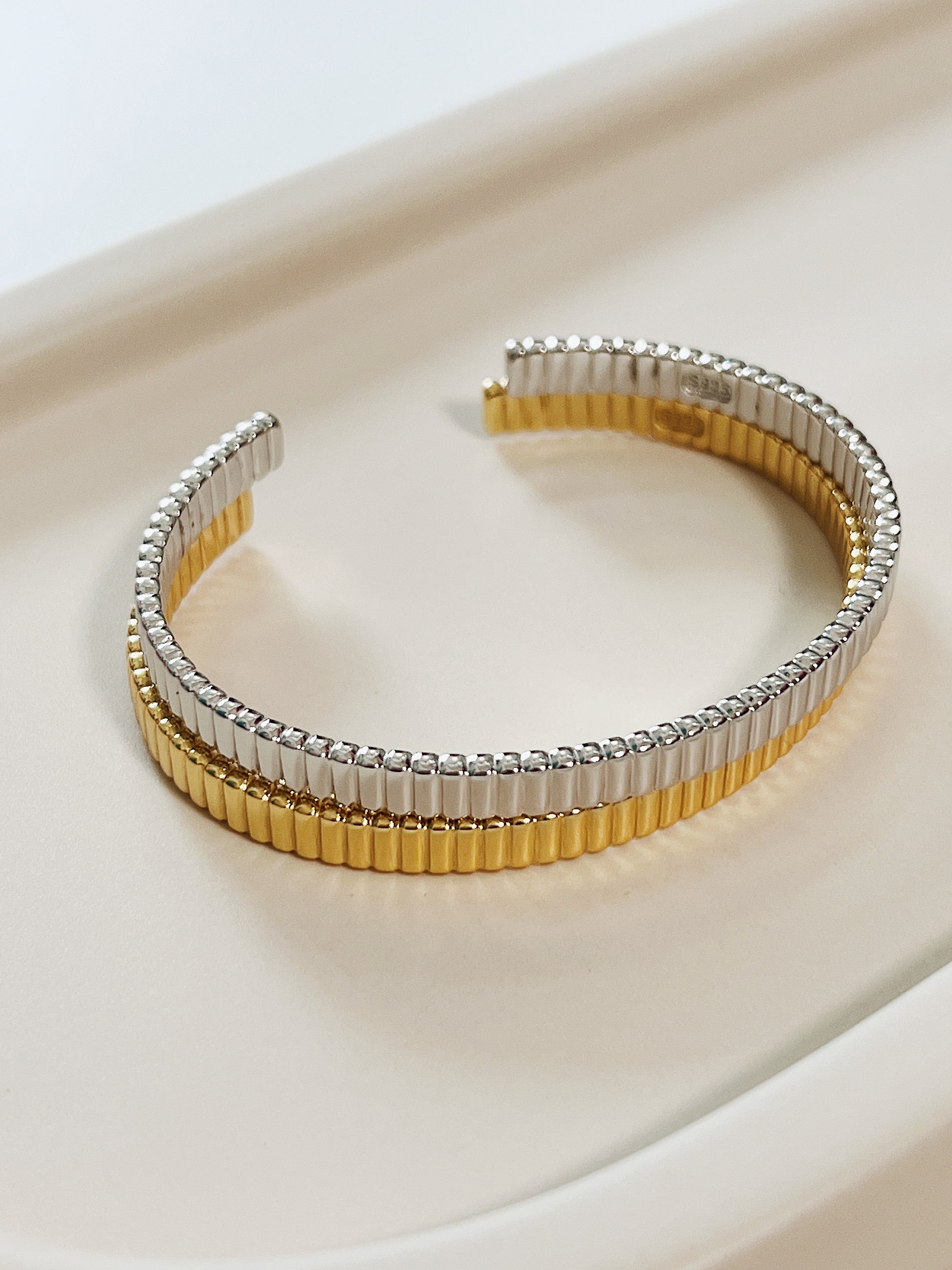 Studio overview showcasing the Vede ribbed flexi cuff stacking bangle set in both 18K gold vermeil and silver stacked close together on a cream ceramic tray.