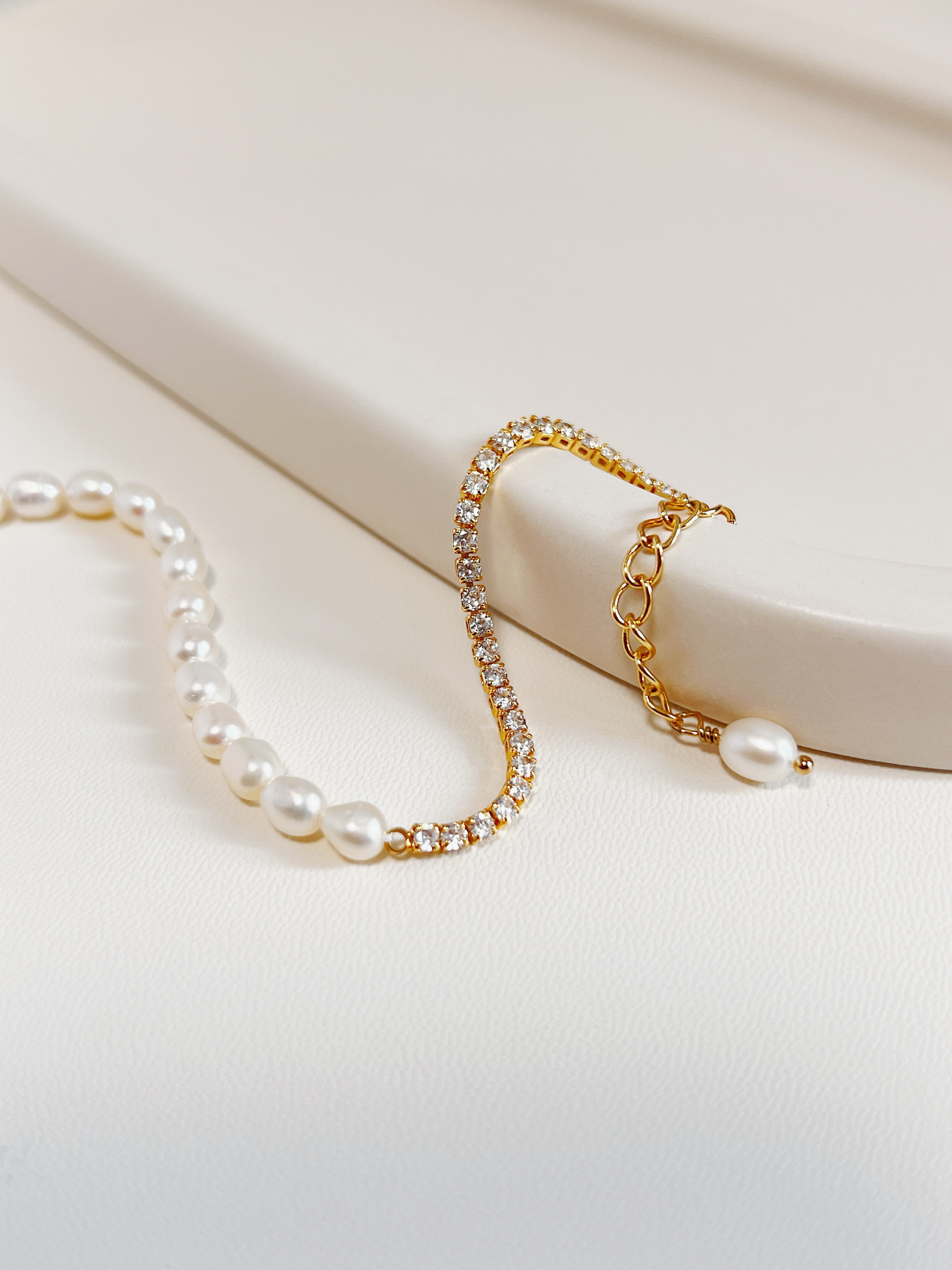 Macro close-up of the gold Vera bracelet curved gracefully over a textured minimalist cream ceramic display tray, showing the continuous high-brilliance micro-set 5A cubic zirconia stones.