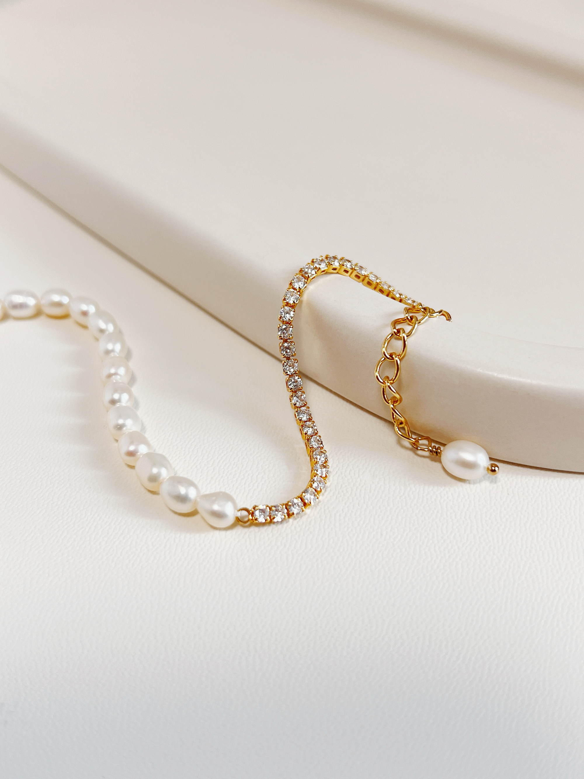 Macro close-up of the gold Vera bracelet curved gracefully over a textured minimalist cream ceramic display tray, showing the continuous high-brilliance micro-set 5A cubic zirconia stones.
