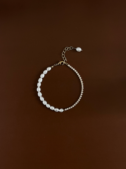 Top-down studio shot of the Vera asymmetric pearl and crystal tennis chain bracelet on a deep brown backdrop, highlighting the high-security gold lobster clasp and extension link.
