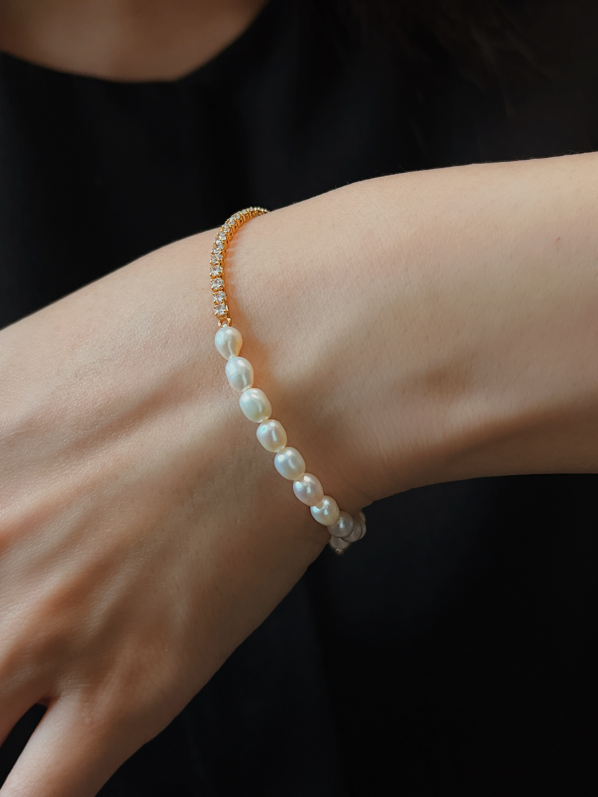On-model styling view of the Vera Half Pearl Half Tennis Chain Bracelet on a wrist against a black top, showcasing the soft organic freshwater pearl strand facing outward.