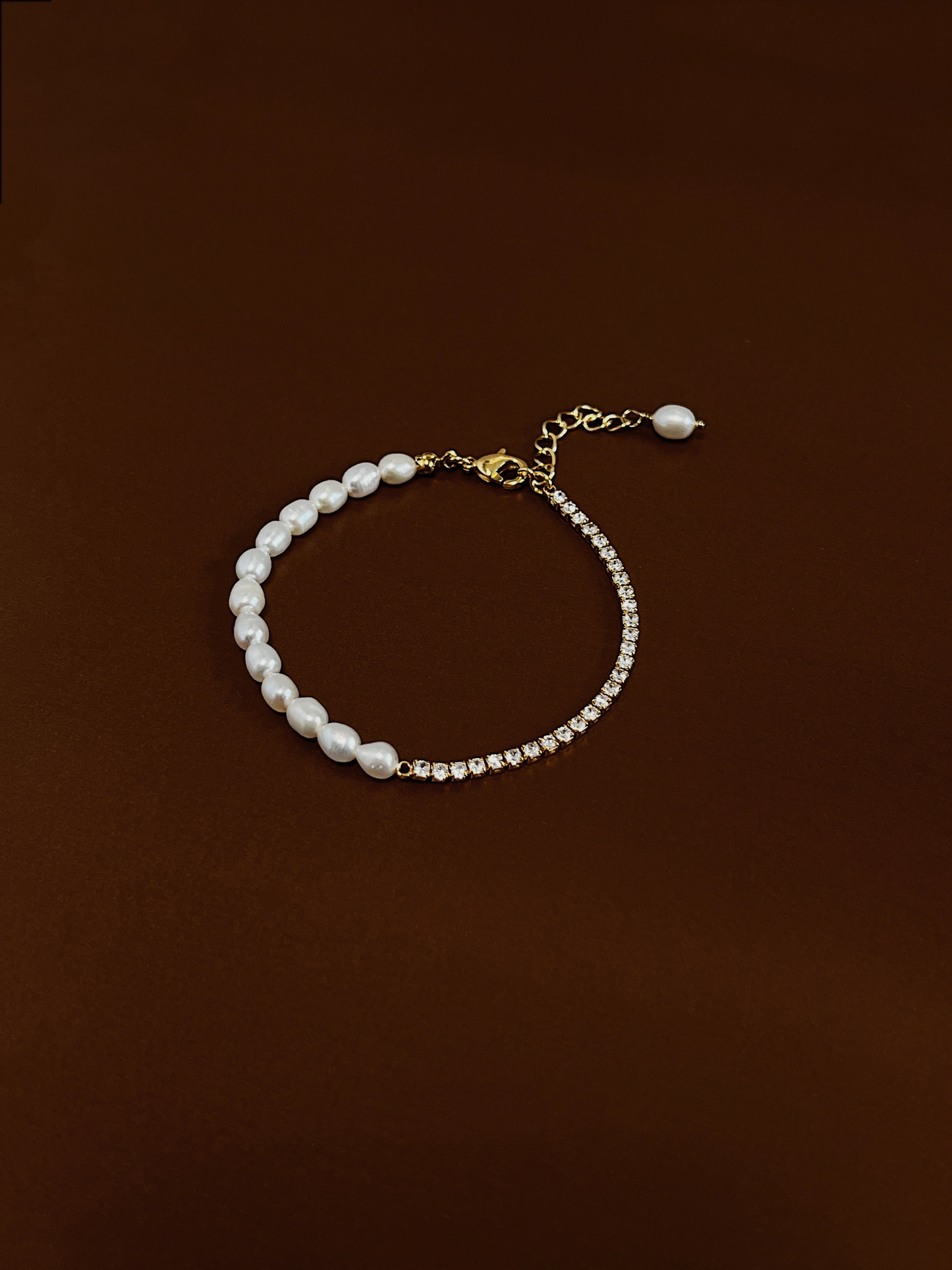Vera Half Pearl Half Tennis Chain Bracelet laid out in a clean circular profile against a rich, dark chocolate brown background, showcasing the exact layout of organic freshwater pearls meeting 5A cubic zirconia stones.
