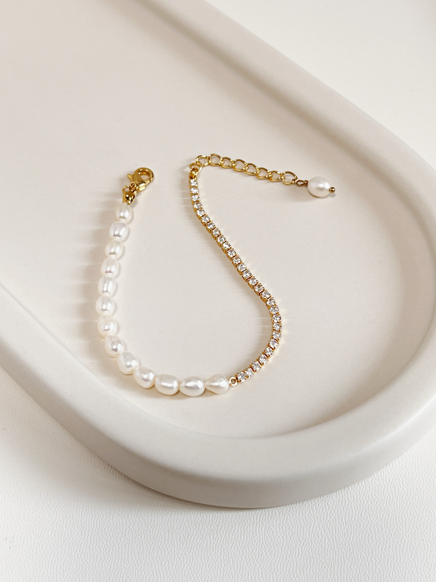 Full overview of the Vera Half Pearl Half Tennis Chain Bracelet resting flat on a modern off-white lifestyle tray, highlighting the fluid drape of the structural gold chain and unique pearl droplet extension end.
