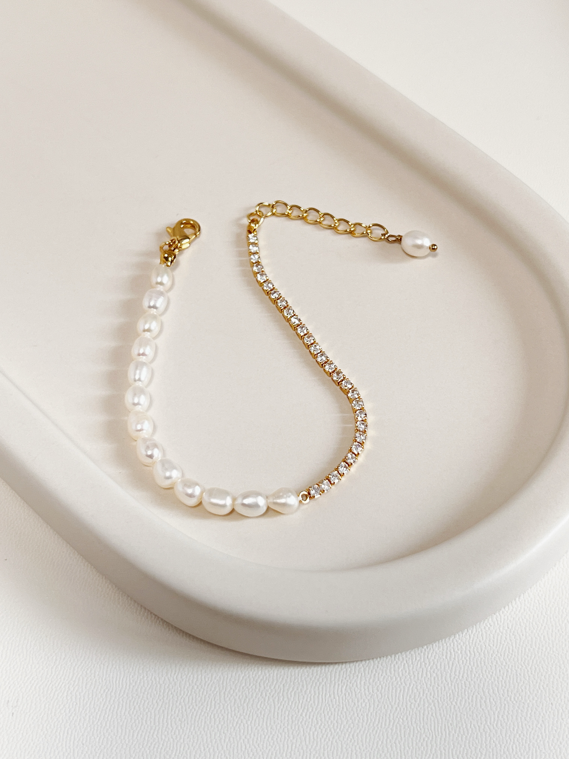 Full overview of the Vera Half Pearl Half Tennis Chain Bracelet resting flat on a modern off-white lifestyle tray, highlighting the fluid drape of the structural gold chain and unique pearl droplet extension end.