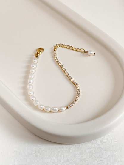 Full overview of the Vera Half Pearl Half Tennis Chain Bracelet resting flat on a modern off-white lifestyle tray, highlighting the fluid drape of the structural gold chain and unique pearl droplet extension end.