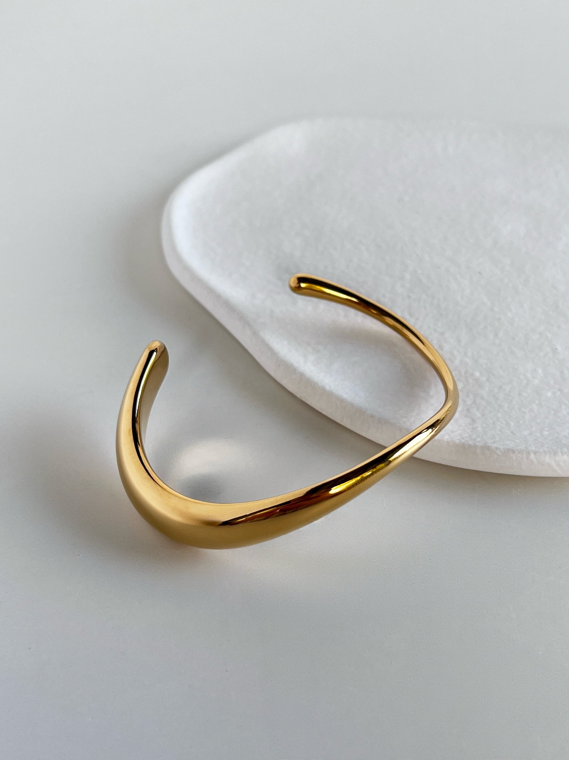 Studio product view showcasing how the Vicky bangle flows seamlessly from a thin gold wire into an expanded sculptural wave focal point.