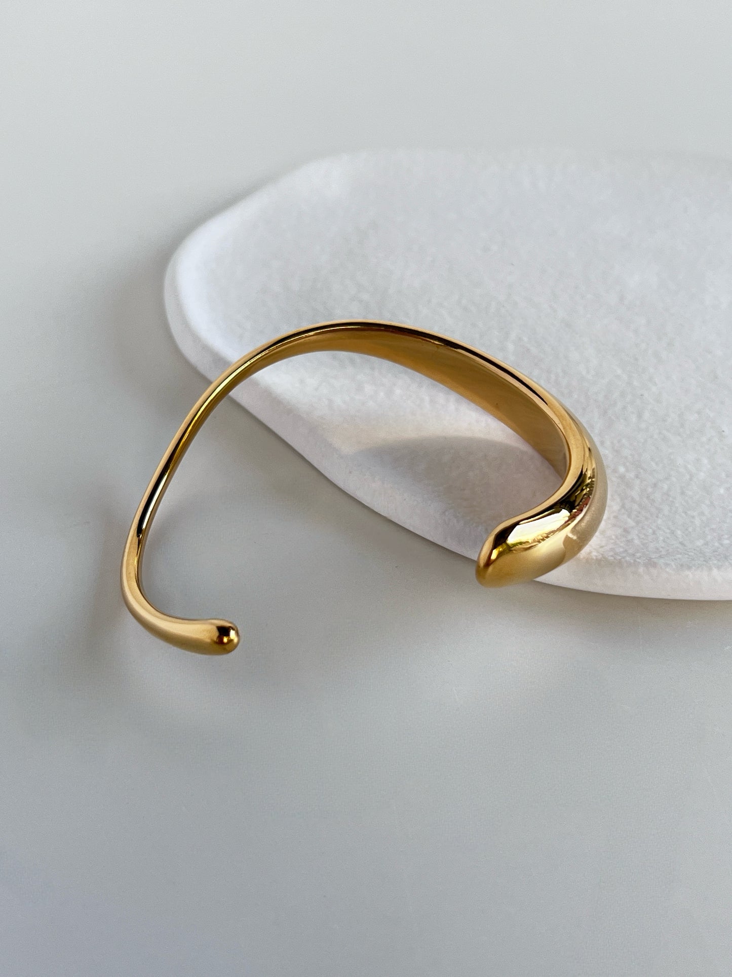 Close-up product shot focusing on the liquid-teardrop thickening of the Vicky gold cuff on an organic display tray, showcasing the reflective mirror polish.