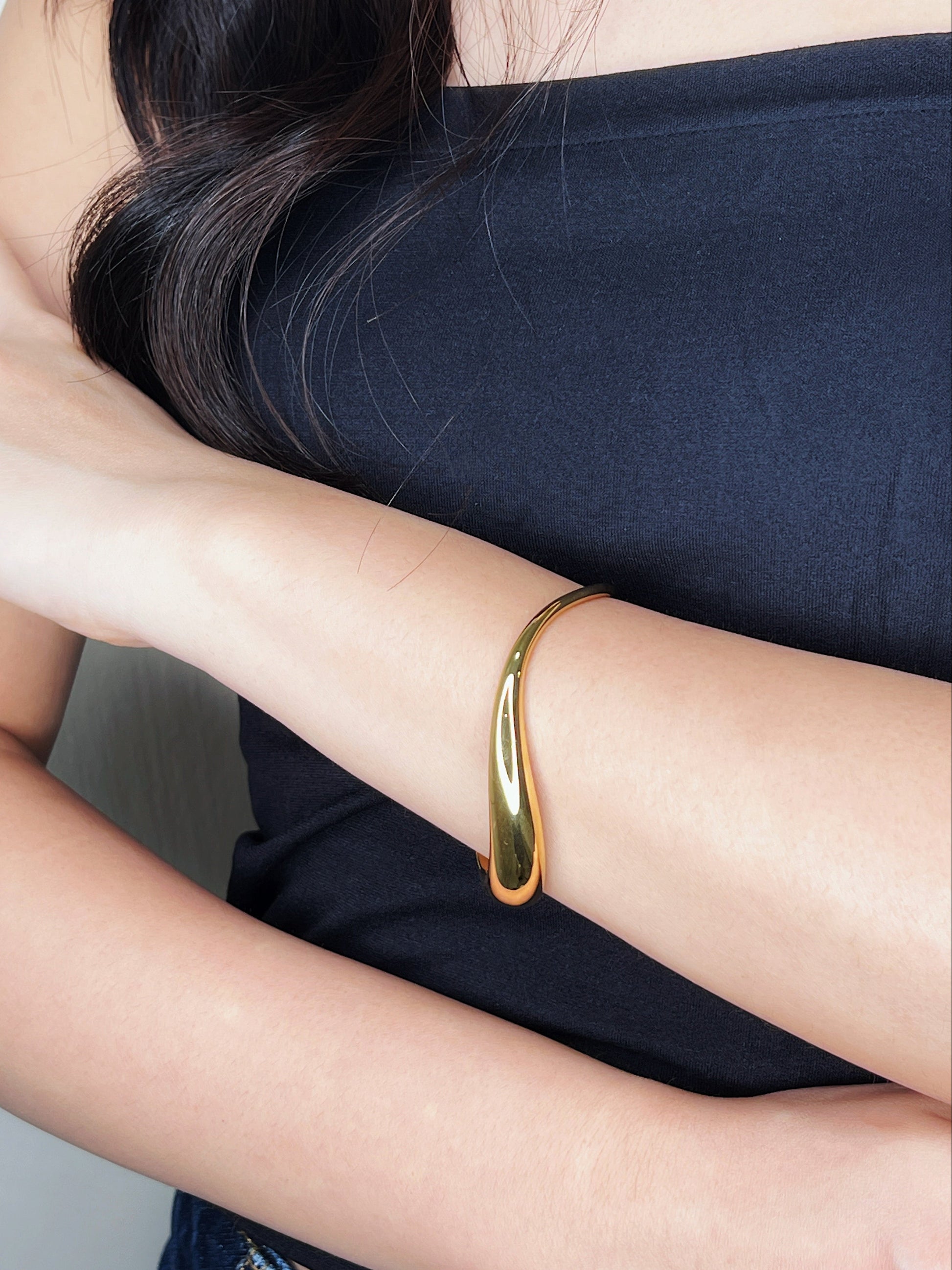 Model styling shot highlighting the elegant side profile of the Vicky gold wave cuff resting comfortably on the wrist against a dark black top,