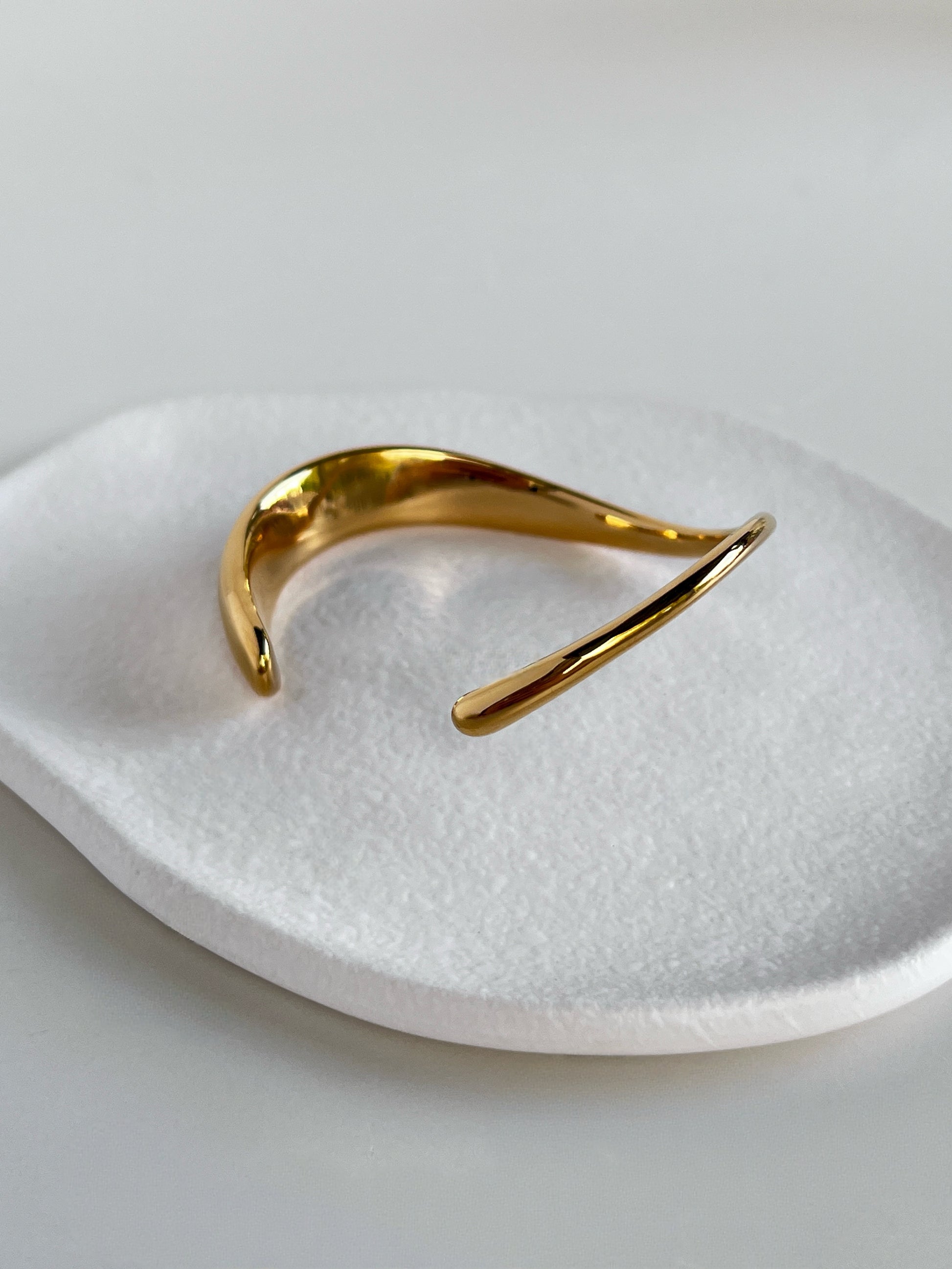 Studio detail shot capturing light reflecting off the mirror-shone surface of the Vicky wave bangle against a neutral studio background.