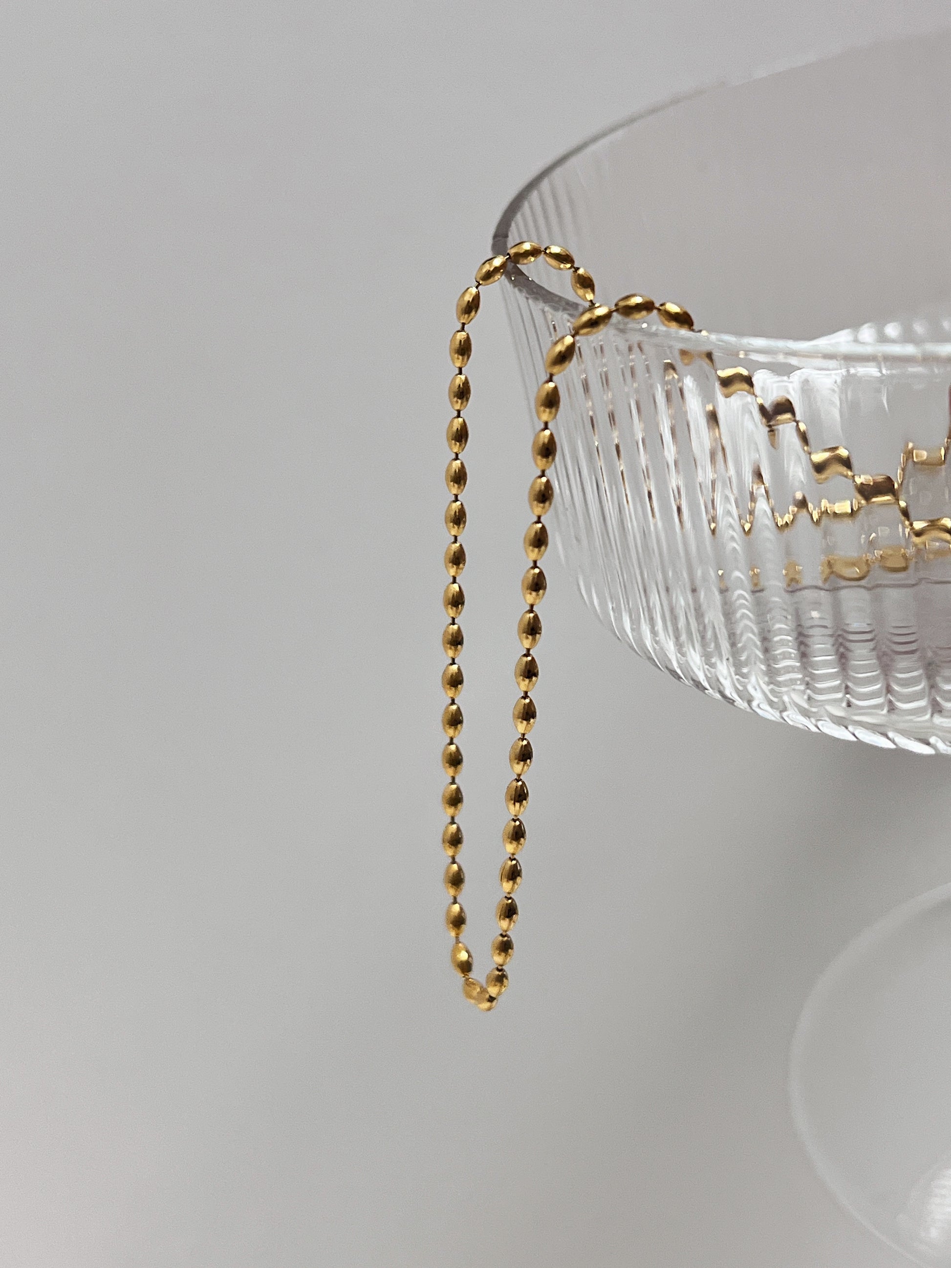Bespoke studio asset showing a fine gold beaded necklet reflecting soft ambient light
