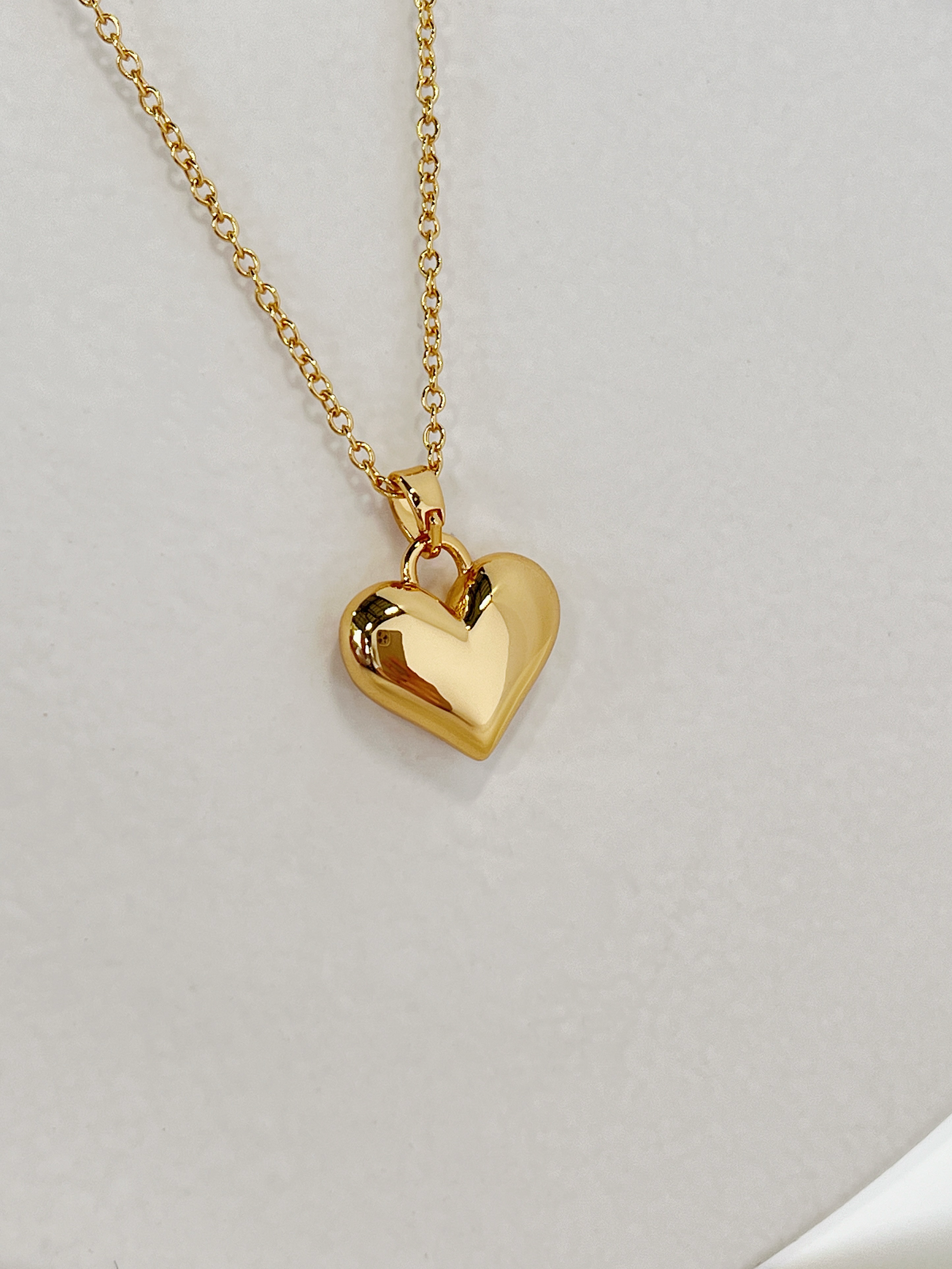 The volumetric solid heart necklace laid out neatly in a looping frame to showcase its fluid chain drape against a clean neutral background