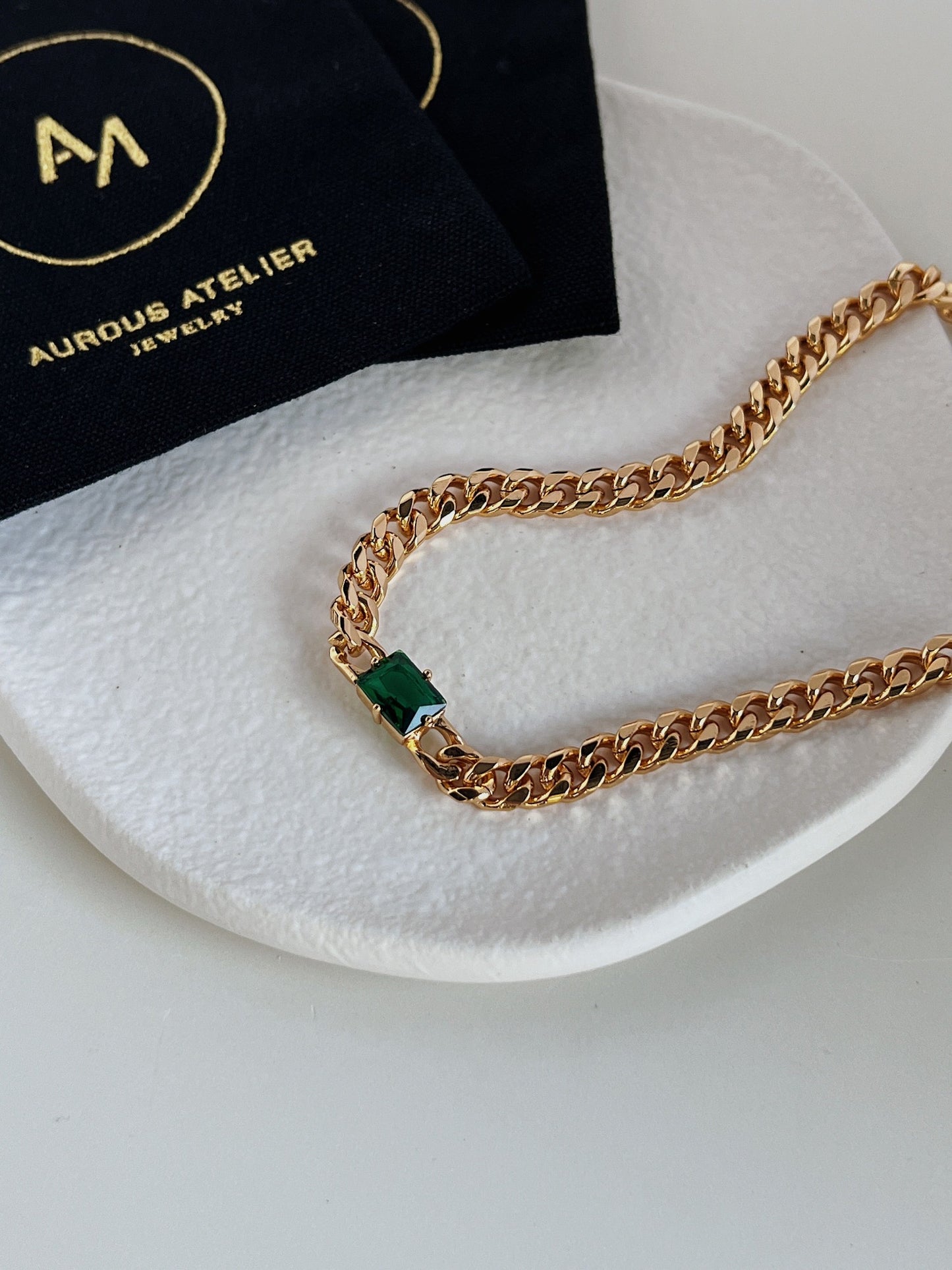 Close up of deep forest green emerald cut gemstone secured in thick gold bezel