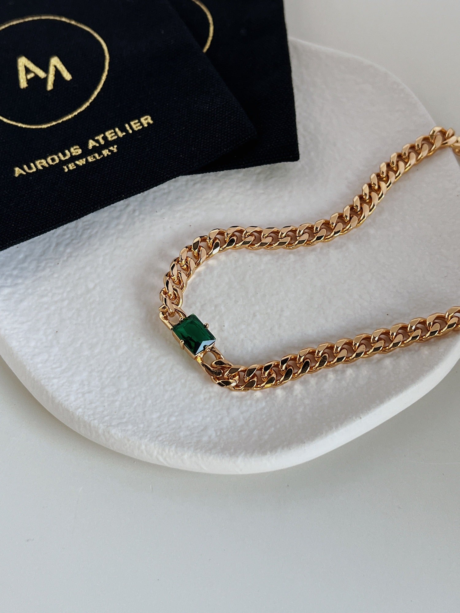 Close up of deep forest green emerald cut gemstone secured in thick gold bezel