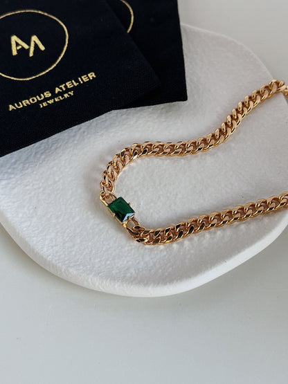 Close up of deep forest green emerald cut gemstone secured in thick gold bezel