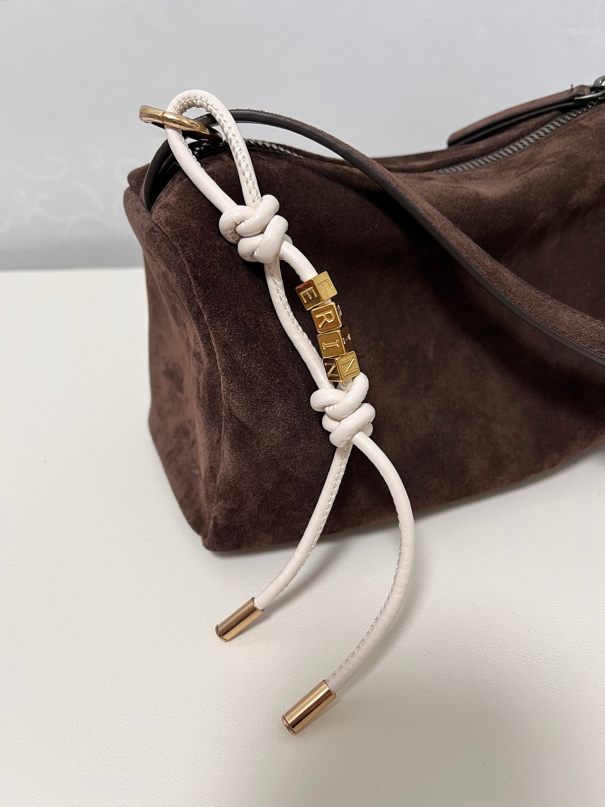 Close-up of initial charm hanging from bag handle.