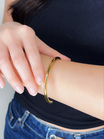 Close-up wrist curation showing the Ines gold stainless steel bracelet paired with a dark neutral outfit for a quiet luxury style statement.