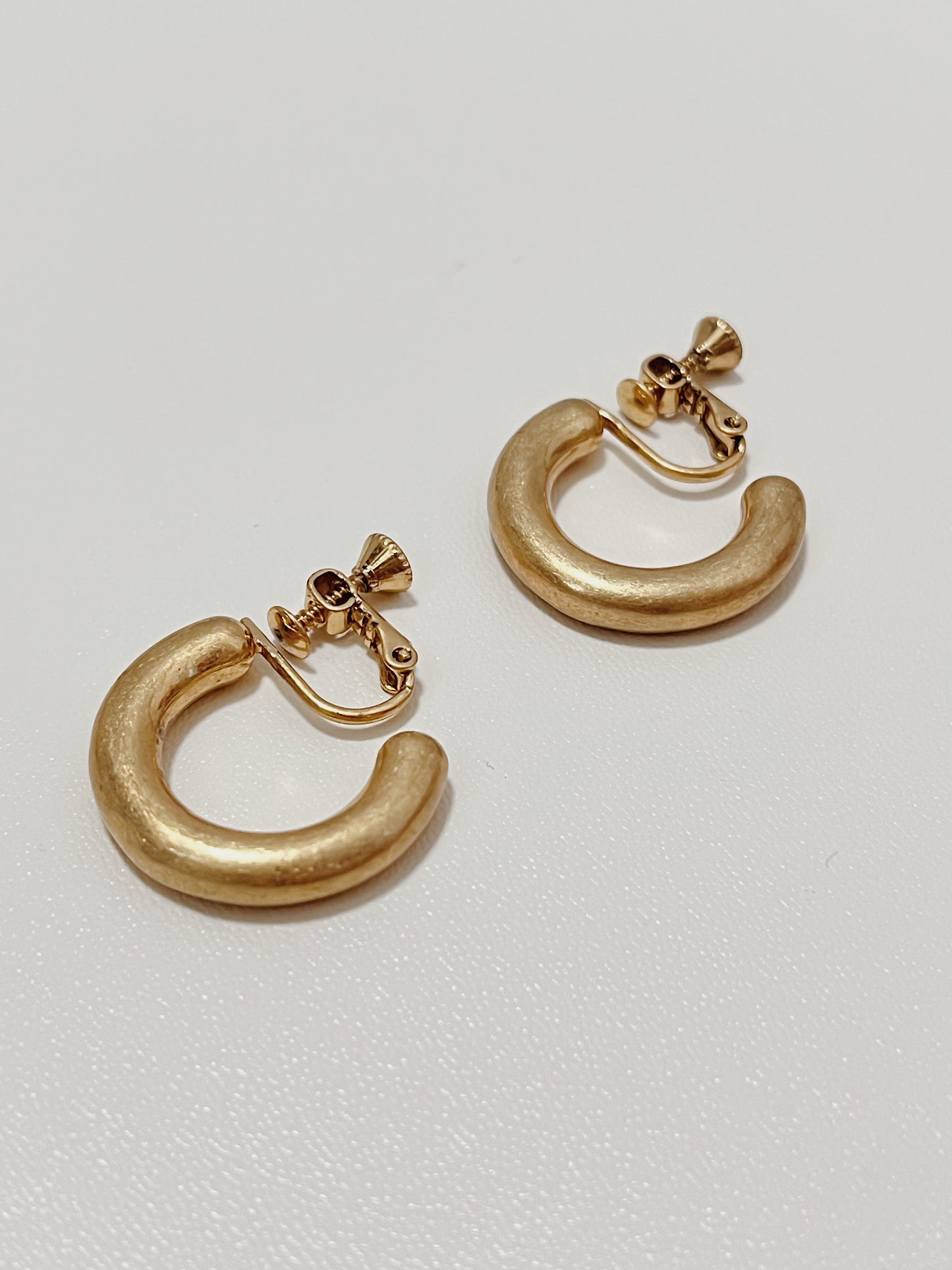 Flatlay view of Zora textured gold clip-on hoop earrings showing the custom matte finish against a clean white backdrop.