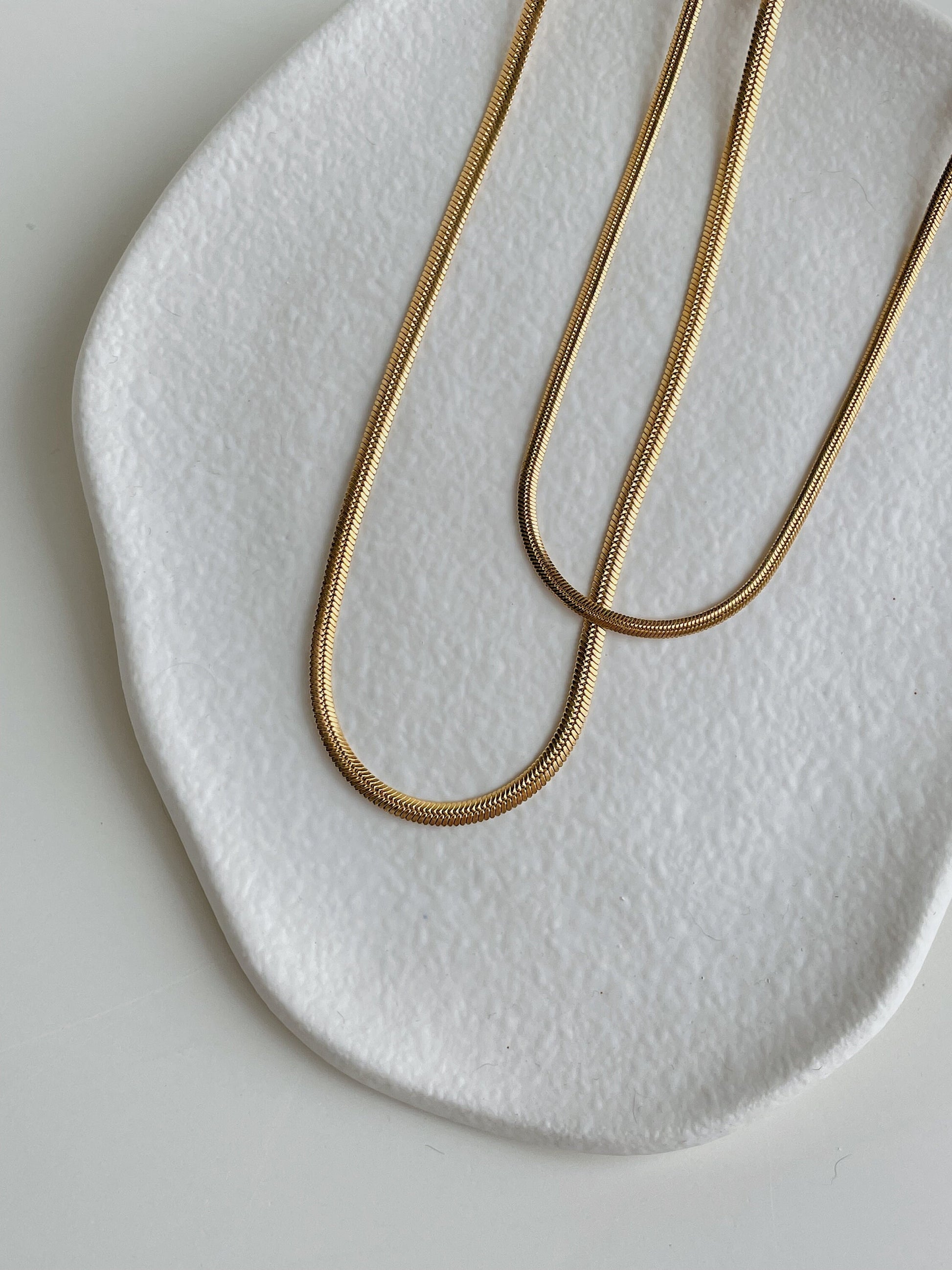 Lola double strand herringbone necklace draped over edge of white surface, natural light, luxury minimal styling