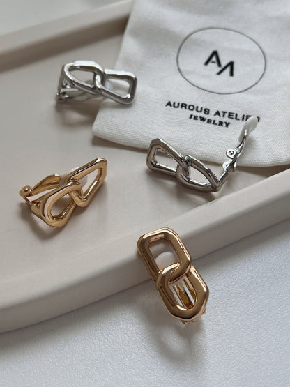 Pair of 18k gold plated and rhodium plated dual rectangular link clip-on earrings with high-shine mirror polish displayed alongside an ivory Aurous Atelier linen pouch.