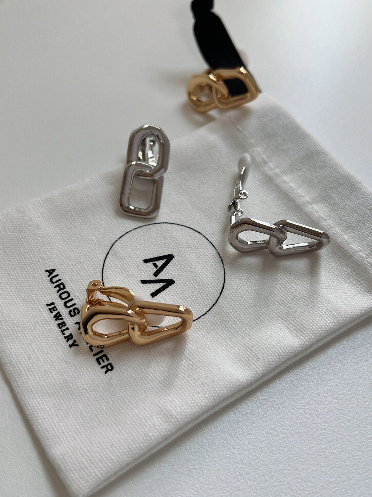 Gold and silver link clip-on earrings arranged on a white jewelry pouch for an understated modern jewelry flatlay.