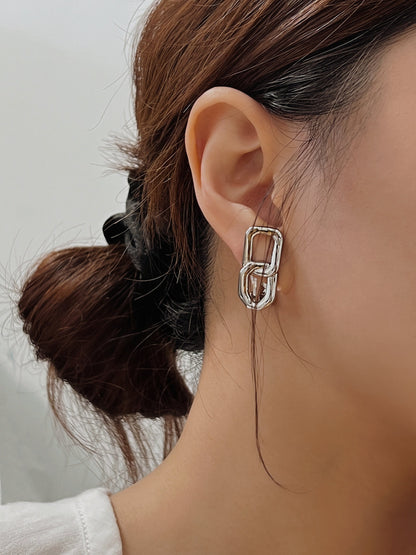 Model wearing silver interlocking link clip-on earrings paired with a soft white blouse for a Quiet Luxury look.