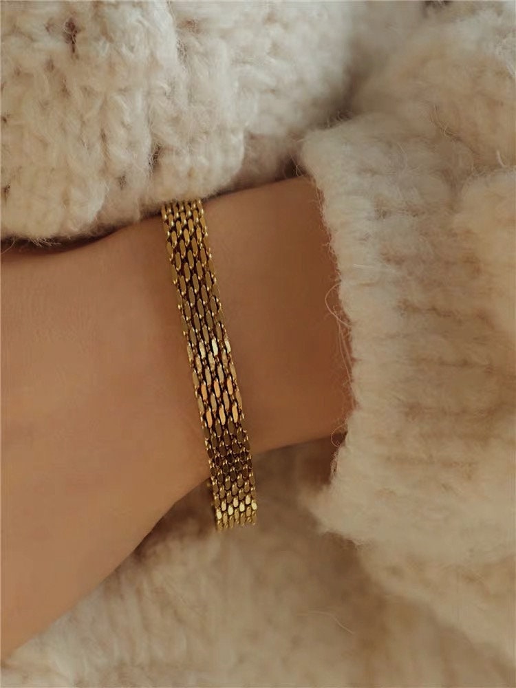 The wide silhouette of the gold Danielle mesh chain bracelet displayed elegantly on a model's wrist as she rests her arm over a neutral fabric.