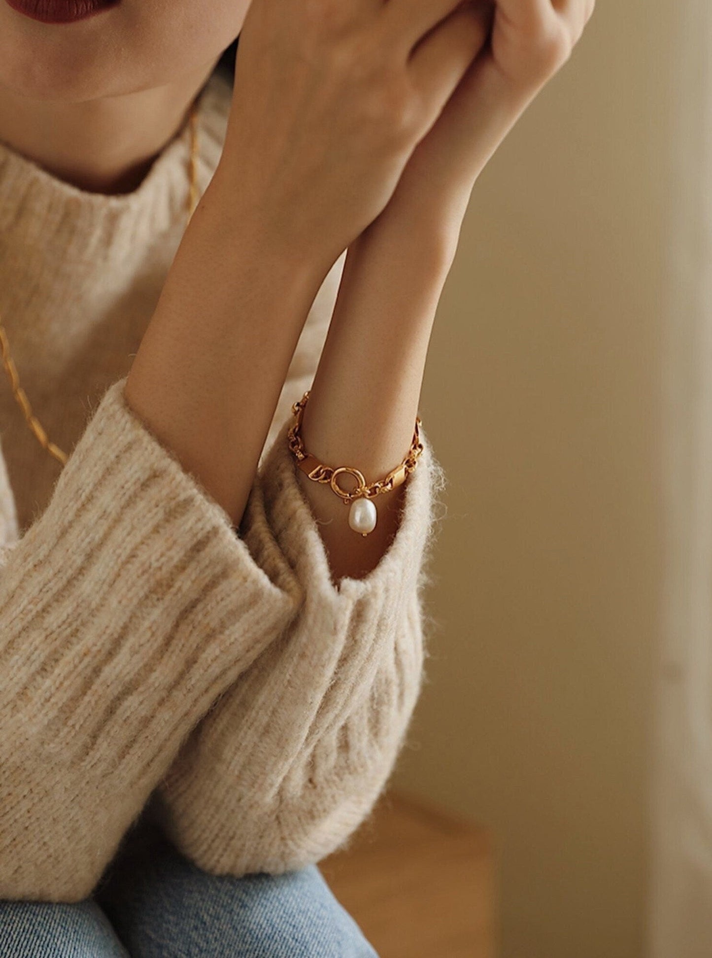 The elegant dangle profile of the baroque pearl drop on the Diana gold chain bracelet as a model rests her arms together.