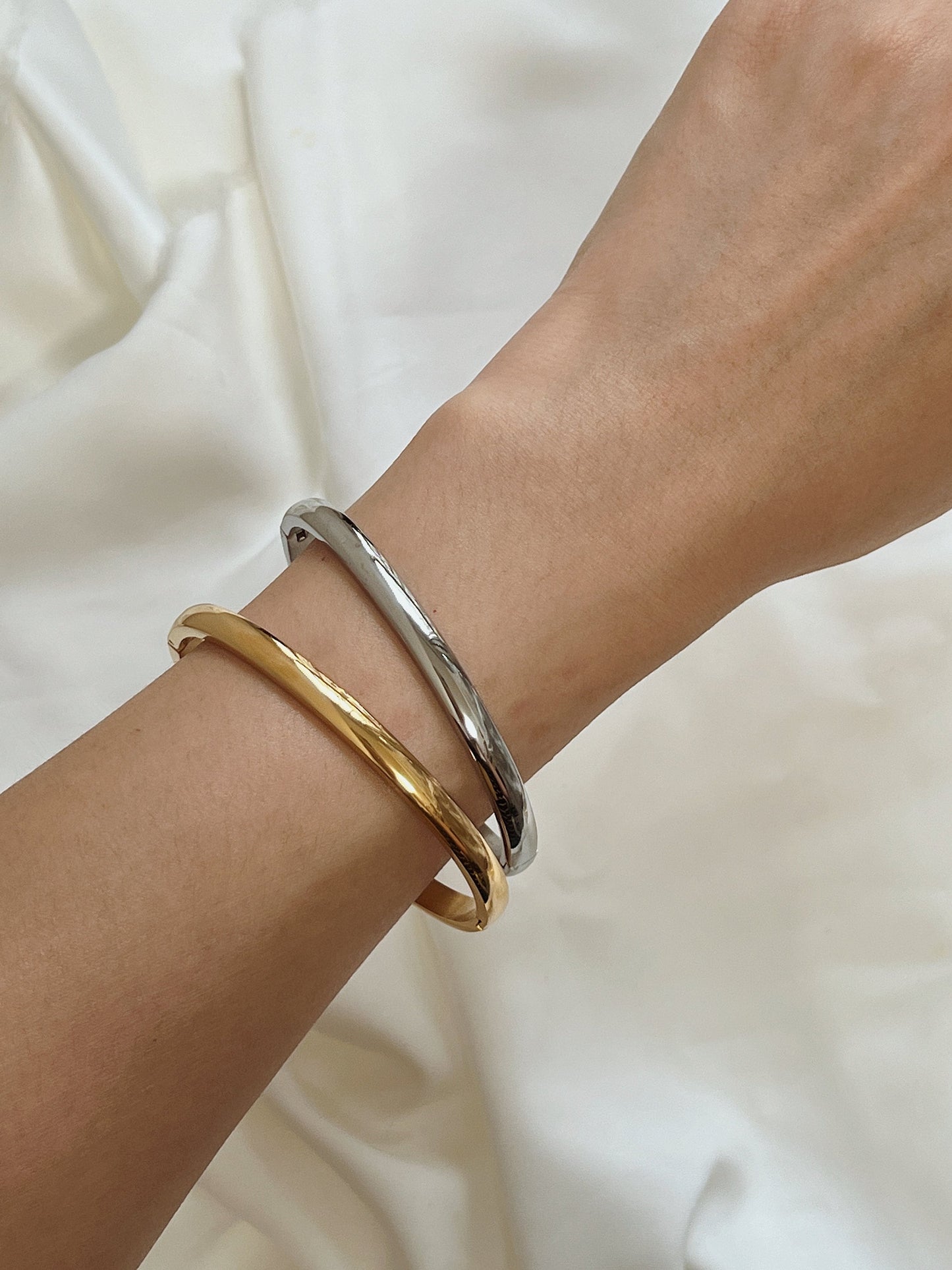 Minimalist wrist shot of a model wearing the 18K gold Jayden 4mm curved bangle against neutral linen fabric.