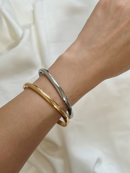 Minimalist wrist shot of a model wearing the 18K gold Jayden 4mm curved bangle against neutral linen fabric.