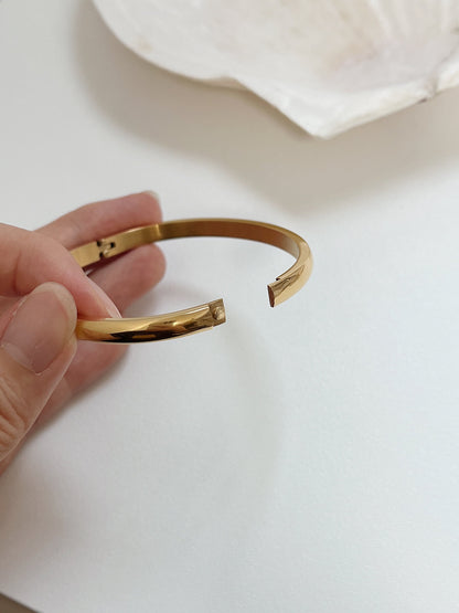 Close-up of the open tension hinge clasp on the 18K gold Jayden oval curved bangle showing internal precision design.