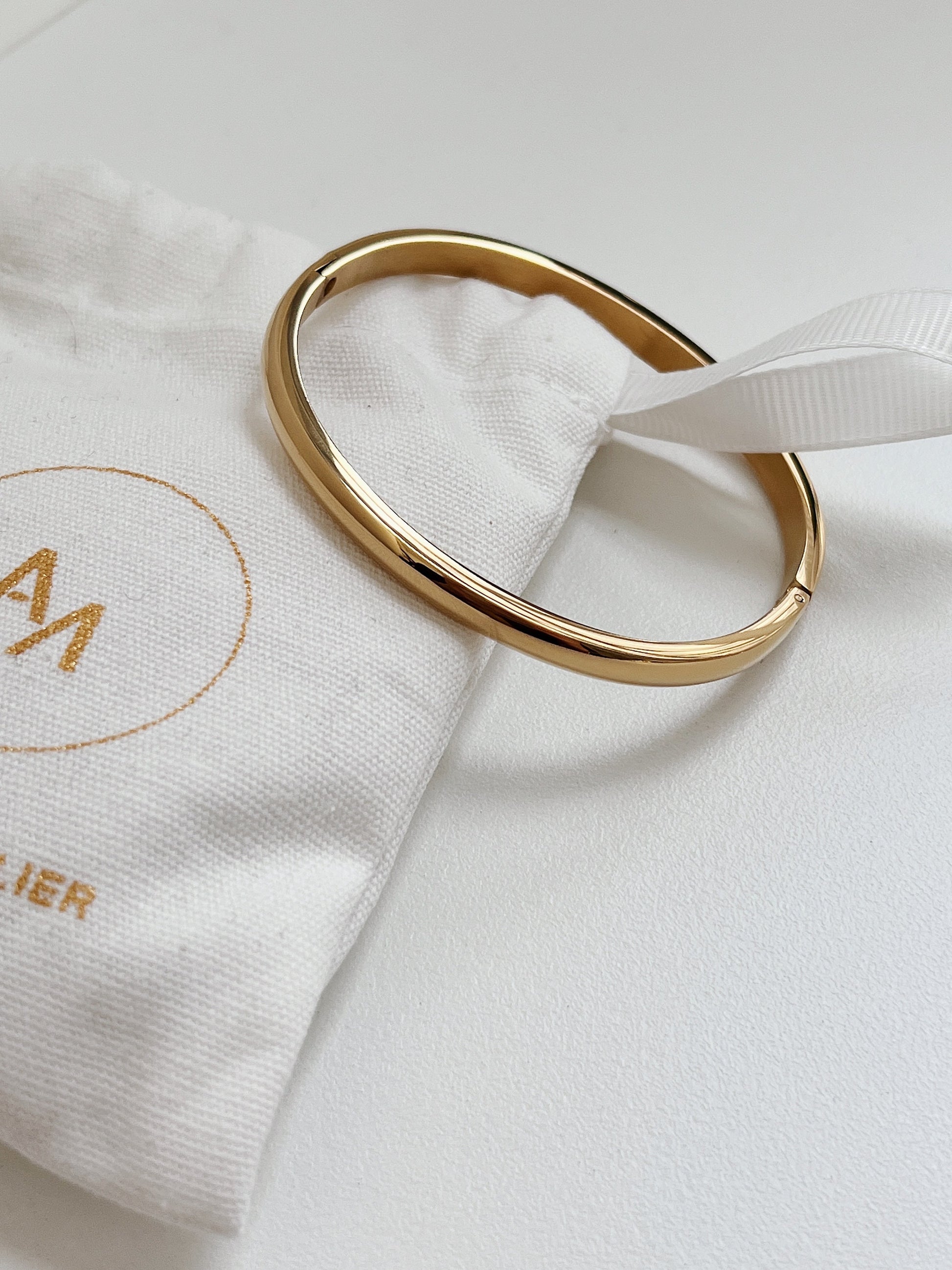 Macro view of the 18K gold Jayden curved oval bangle on an Aurous Atelier cloth drawstring bag.
