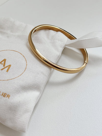 Macro view of the 18K gold Jayden curved oval bangle on an Aurous Atelier cloth drawstring bag.