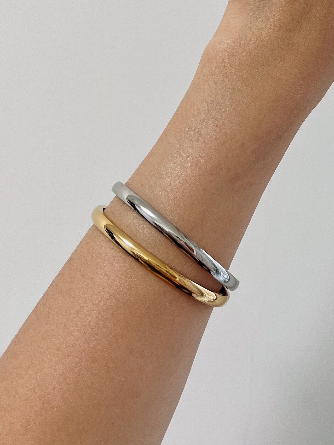 Model wrist wearing the Jayden 18K gold and silver oval bangles stacked together for a modern mixed-metal look.