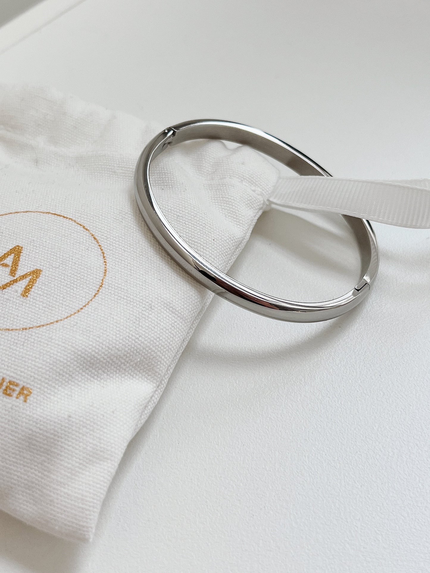 Silver Jayden 4mm smooth oval bangle resting on a branded white linen jewelry pouch.