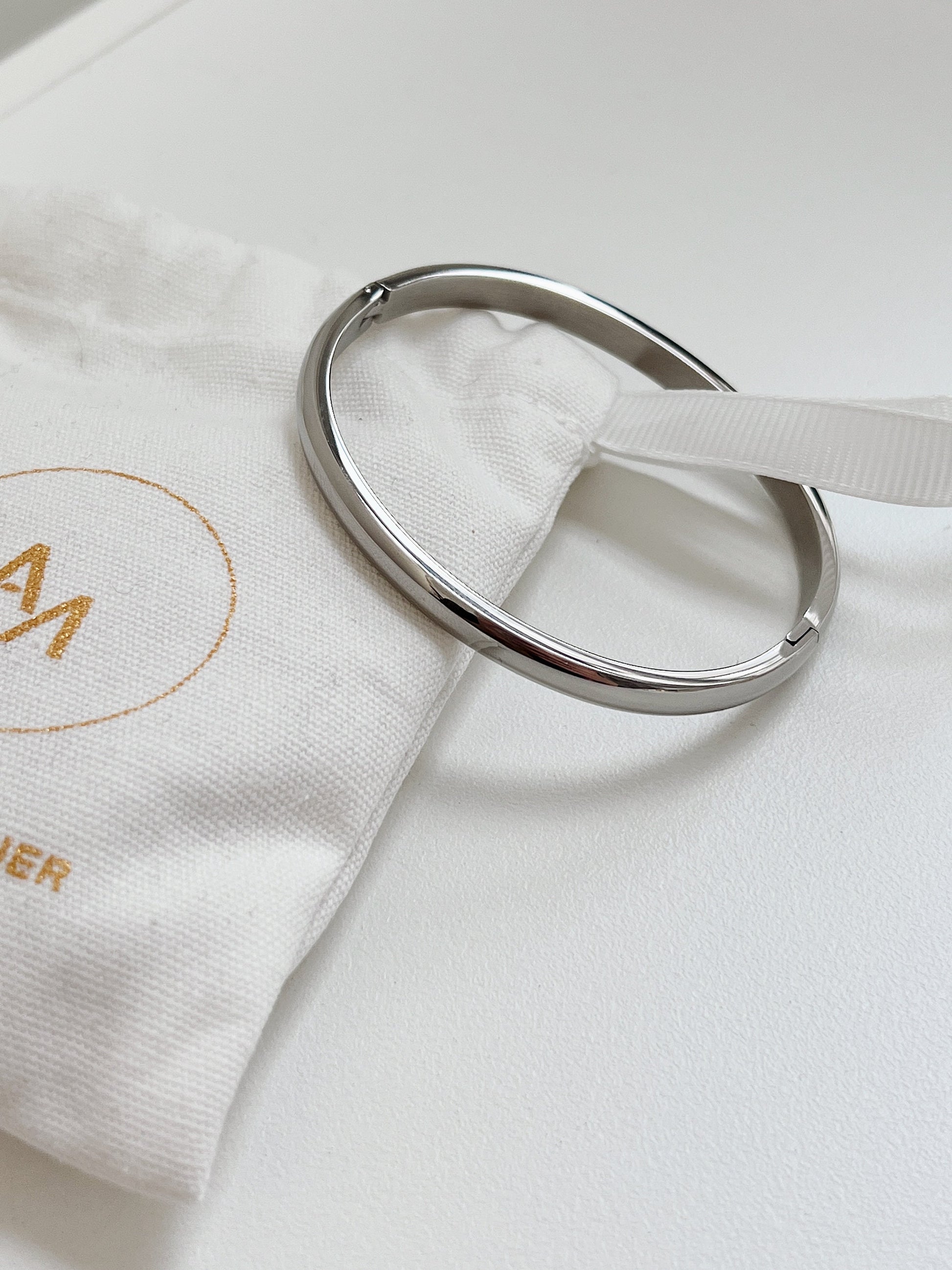 Silver Jayden 4mm smooth oval bangle resting on a branded white linen jewelry pouch.